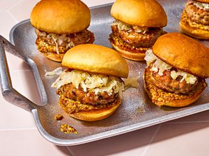 A serving tray with five sauerkraut topped bratwurst sliders