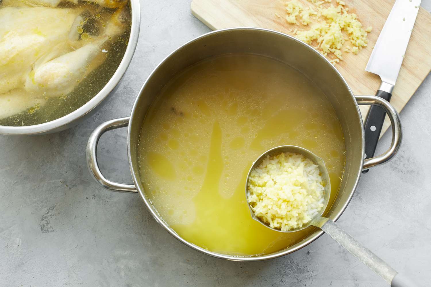 Pot of Chicken Broth with Rice and Minced Ginger Next to Bowl of Chicken and Cutting Board with Minced Ginger for Chào Gá (Vietnamese Rice Porridge) 