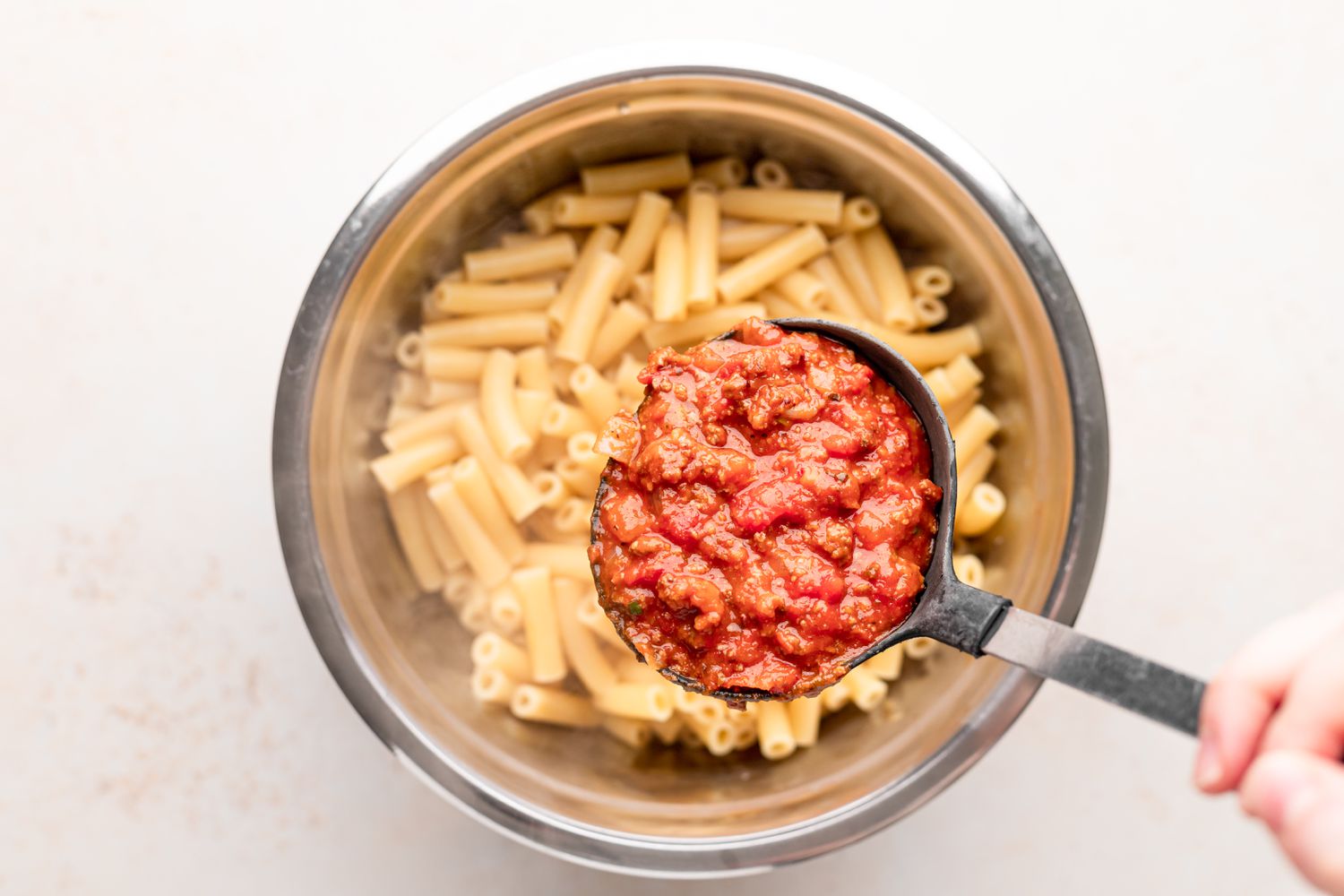 Adding sauce to ziti noodles.