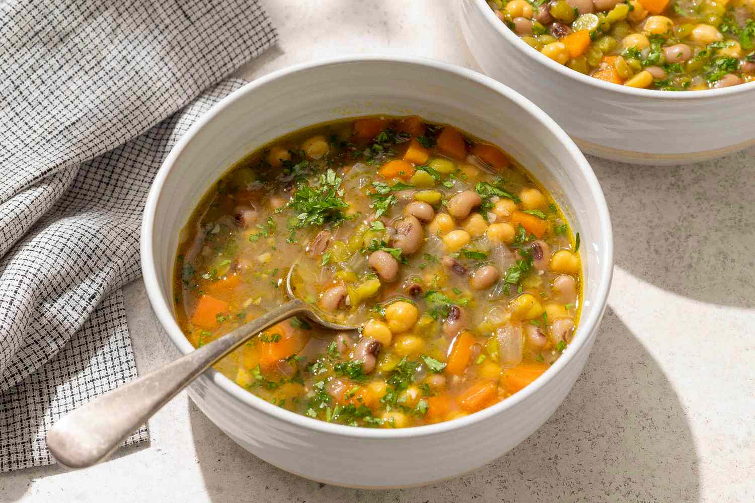 A bowl of pea soup containing vegetables and beans with a spoon