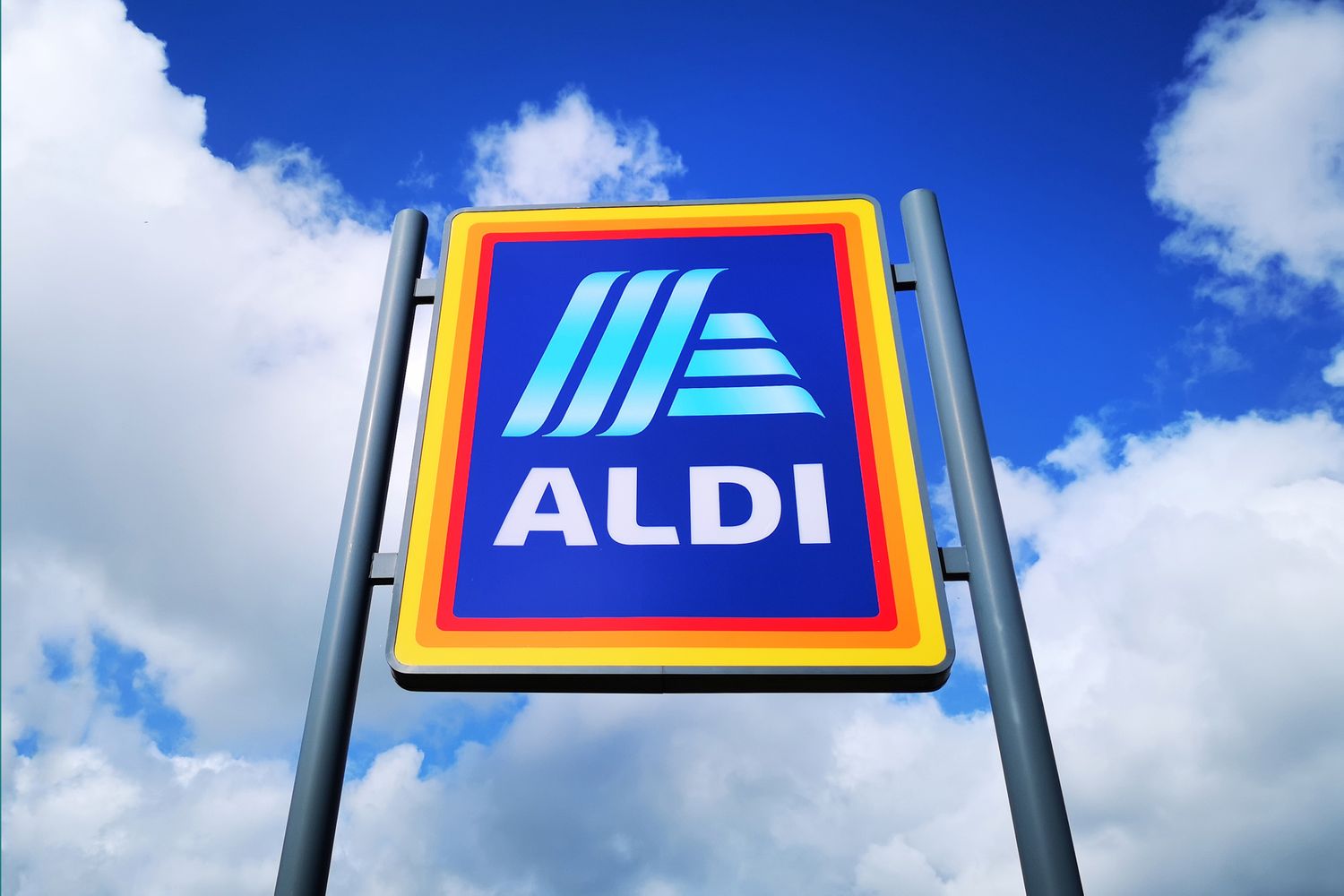 An Aldi logo displayed on a signpost against a background of a cloudy sky