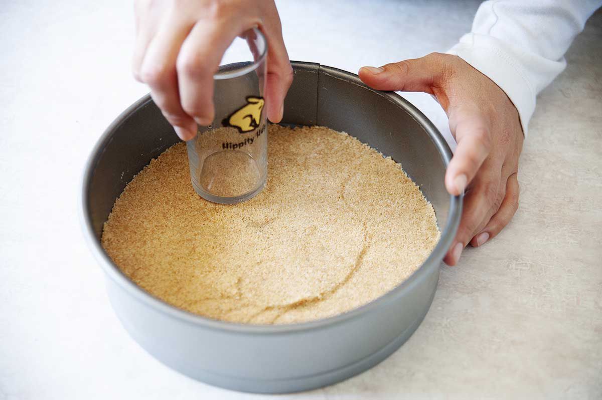 Pressing a graham cracker crust into a springform pan.