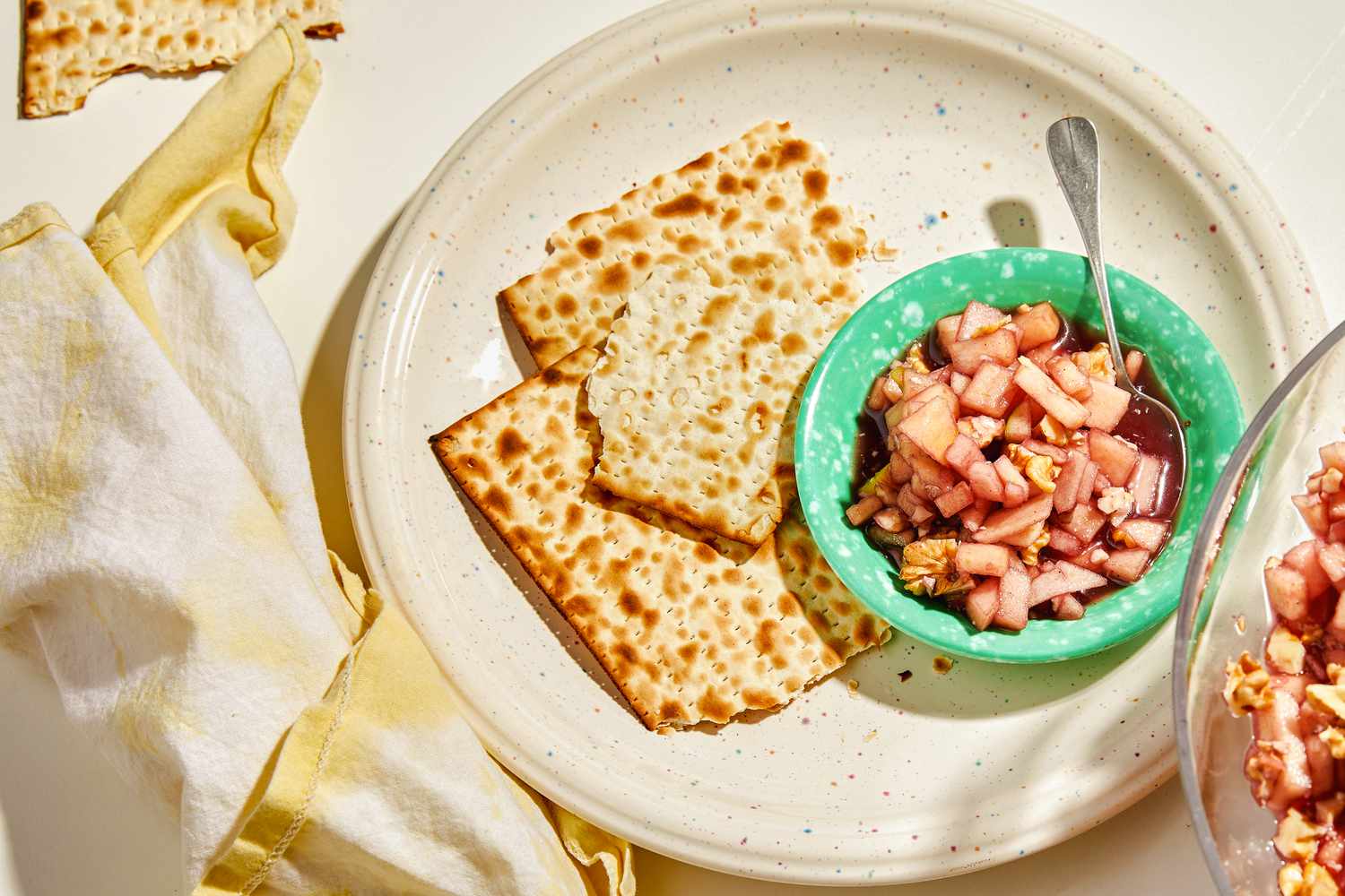 Charoset in a small turquoise dish with a spoon and broken pieces of matzo on the side