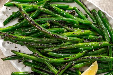 A closeup overhead shot of slightly charred pan fried green beans sprinkled with coarse salt and garnished with a lemon wedge