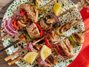 Grilled tuna kebabs with vegetables and lemon slices on a speckled plate