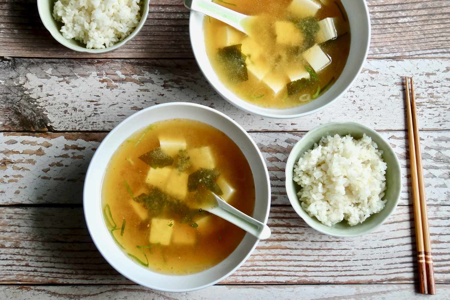 Overhead view of two bowls of homemade miso soup with small bowls of rice next to it.