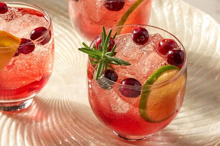 Three cranberry ginger spritz cocktails garnished with cranberries lime slices and a sprig of rosemary
