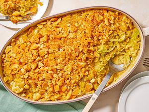 A casserole dish with cheesy cabbage casserole topped with a crunchy layer served with utensils and a green napkin nearby
