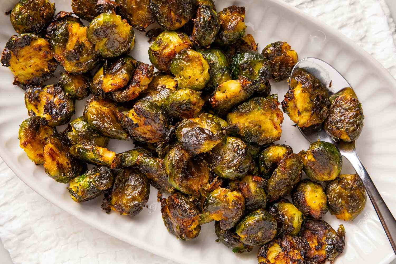 Plate of roasted and seasoned smashed Brussels sprouts with a spoon on the side