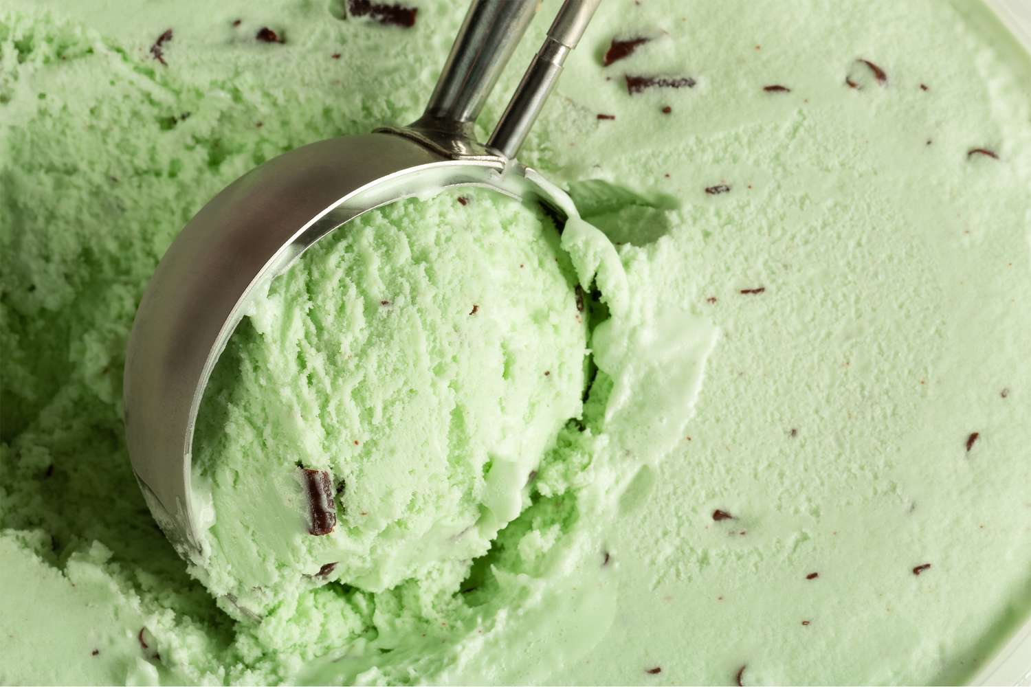 Scooping mint chip ice cream with a metal ice cream scooper visible chocolate shavings on mintflavored ice cream