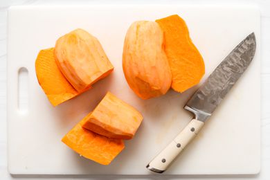 Overhead view of a white cutting board with a large knife and two sliced sweet potatoes