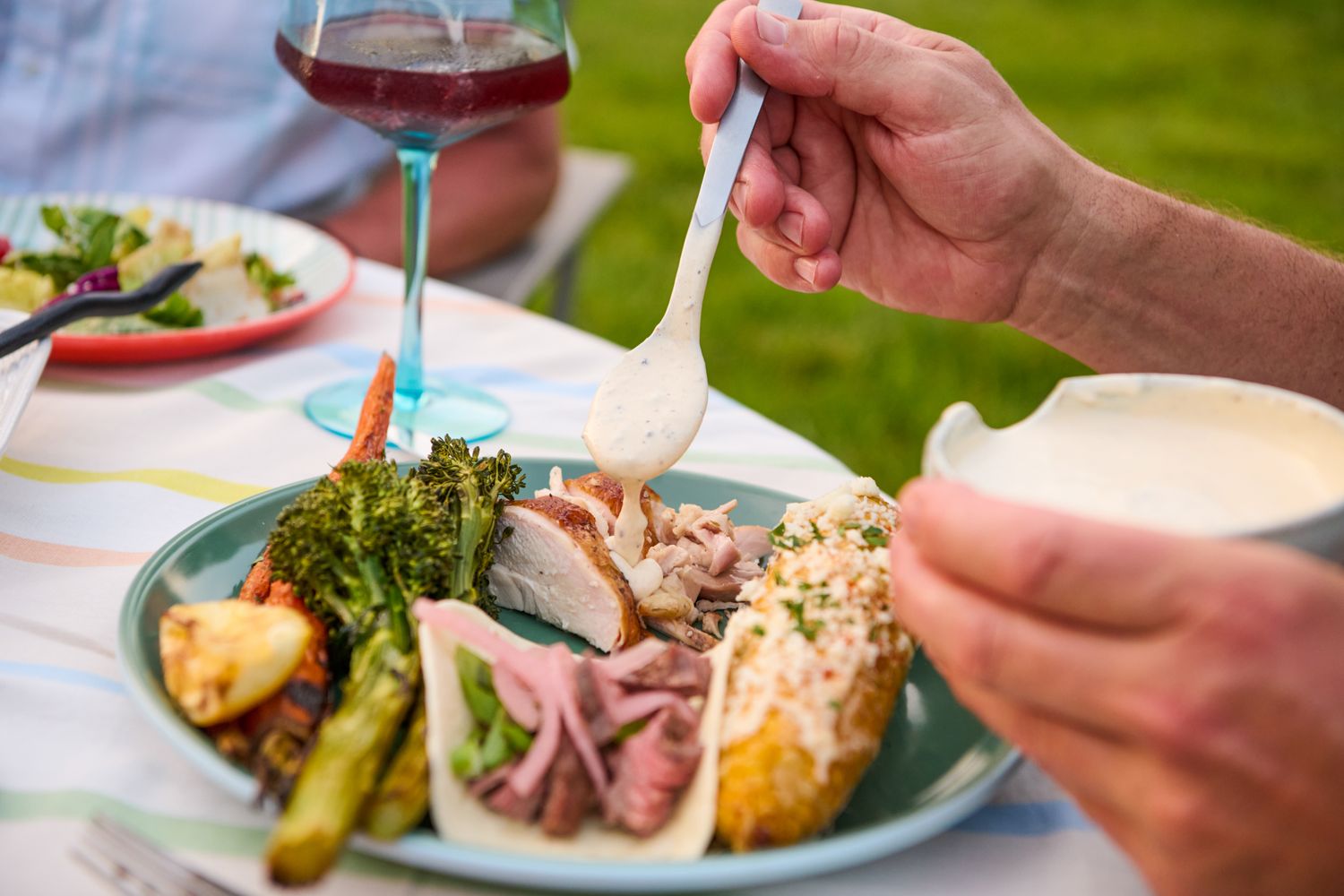 Plate of food being served with Alabama white sauce, including vegetables and meats, a dining setup in an outdoor setting
