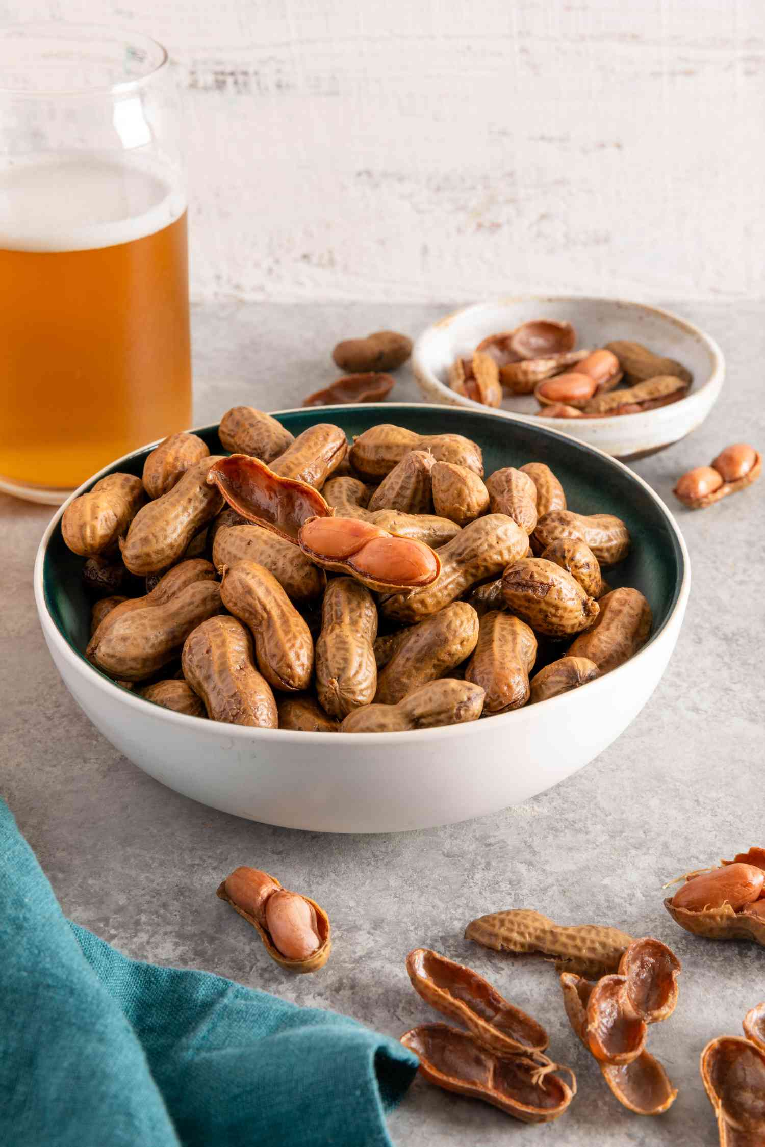 A bowl of boiled peanuts on a table with shelled boiled peanuts and a beer glass in the background