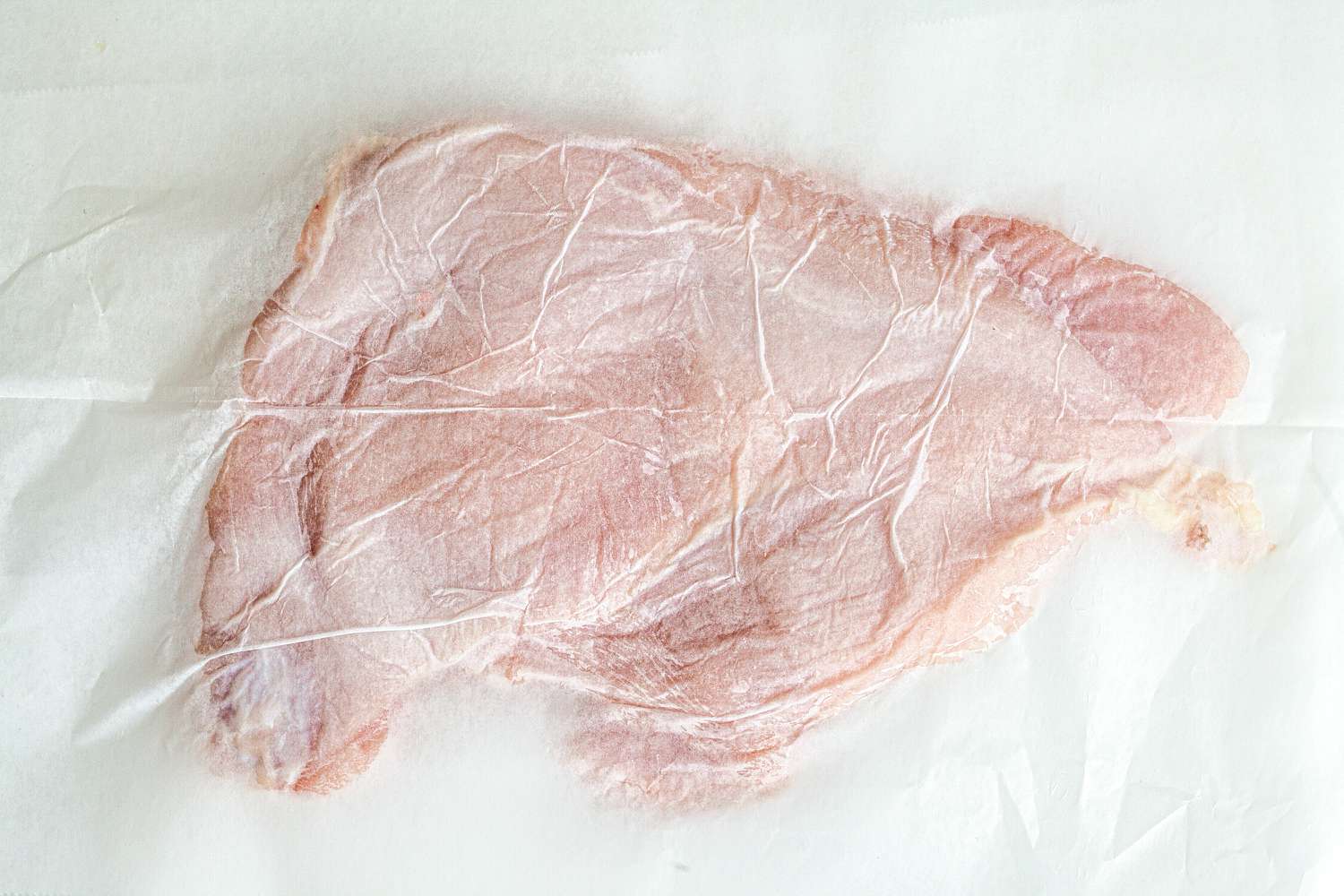 Raw turkey breast flattened for a turkey breast recipe.