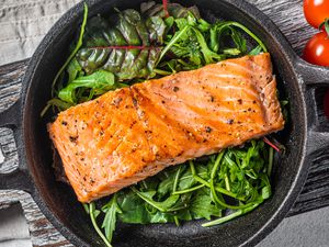 cooked salmon fillet on a bed of mixed greens, all in a small cast iron skillet