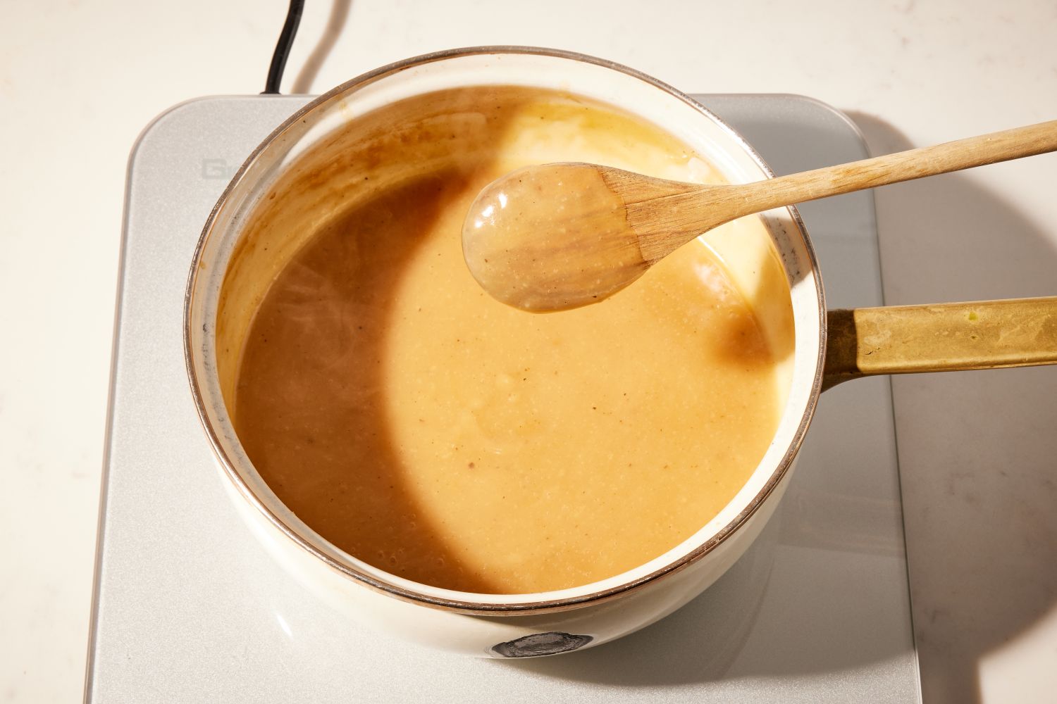 Angled view of a white pot on a hot plate with gravy for Best Ever Gravy recipe