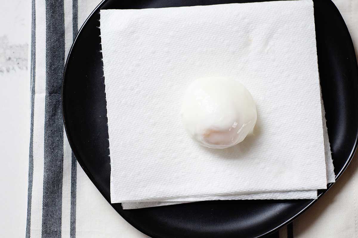 A black plate with simple poached egg draining on a paper towel.