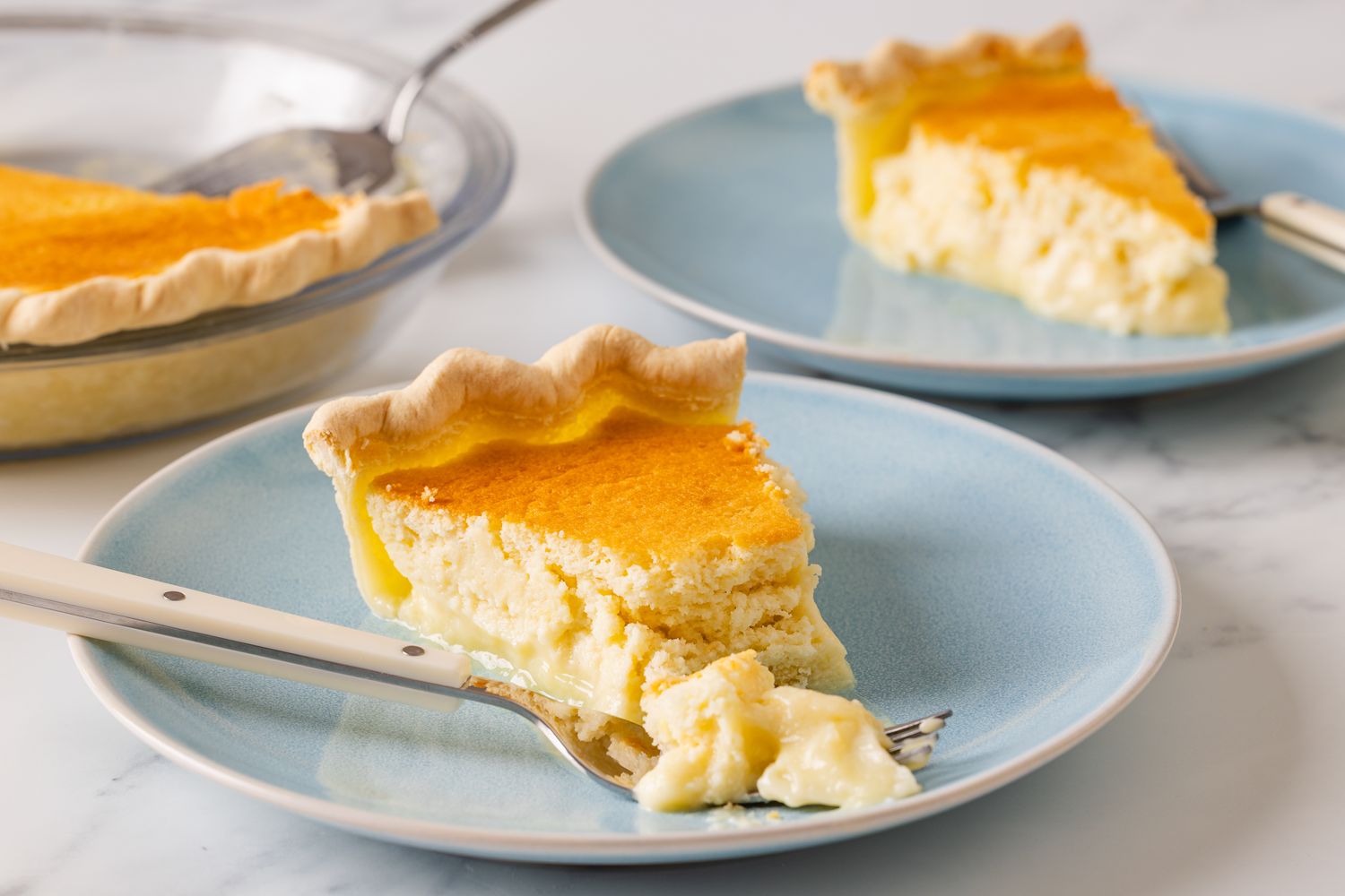 Two slices of lemon pie on blue plates one partially eaten with a fork