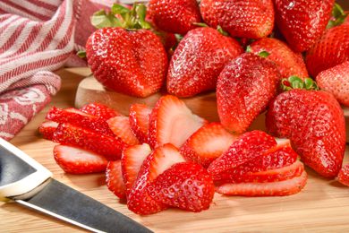 Fresh strawberries, whole and sliced, with a knife on a wooden surface