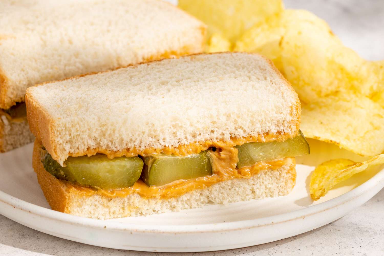 Peanut butter and pickle sandwich on a plate with potato chips