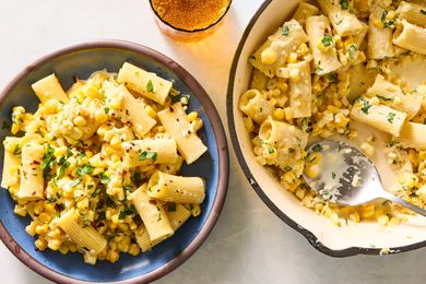 A bowl and a skillet with cooked pasta mixed with corn and garnished with herbs