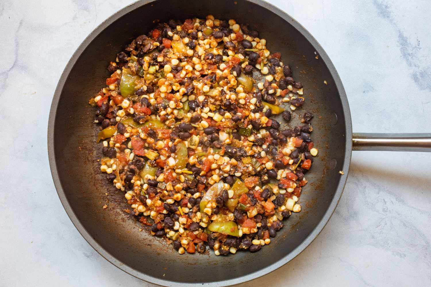 A skillet with black bean mixture to make black bean, corn, and pepper freezer burritos.