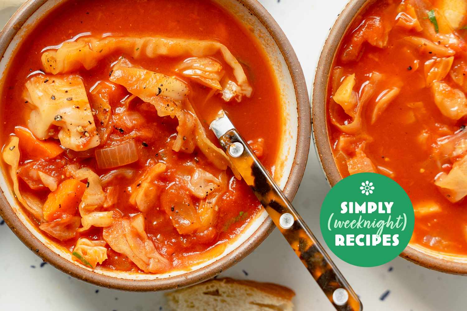 Two bowls of soup with a tomato base and pasta accompanied by bread