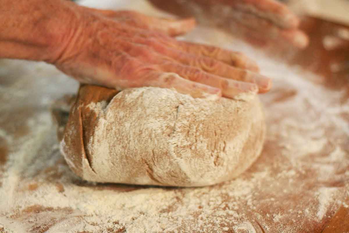 A hand smashing down and shaping rye bread dough
