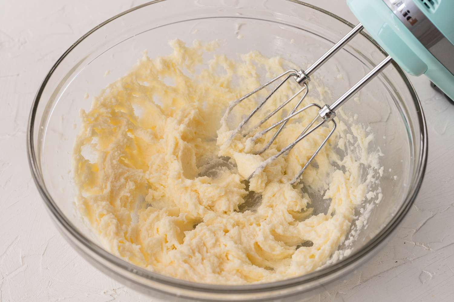A glass bowl with hand mixer mixing ingredients to make a banana cookie recipe.