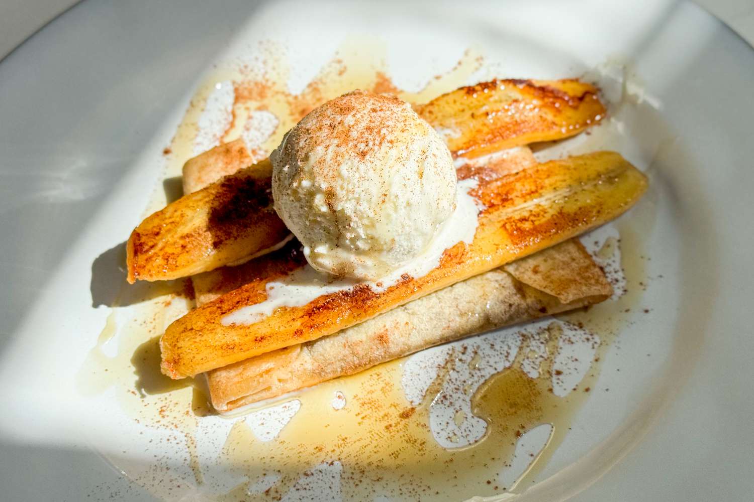 Dessert dish featuring grilled bananas, a tortilla, and a scoop of ice cream, drizzled with syrup