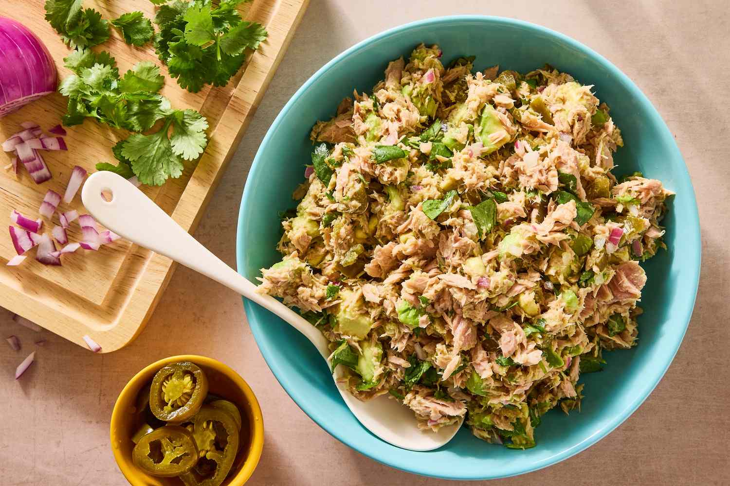 Tuna and avocado salad in a bowl with a spoon sliced jalapeos and herbs near it