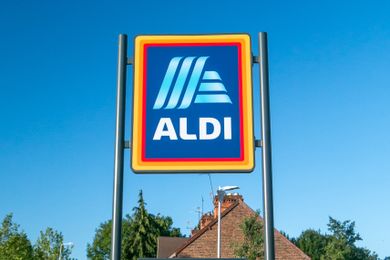A sign with the Aldi logo displayed on a post in front of clear sky and trees