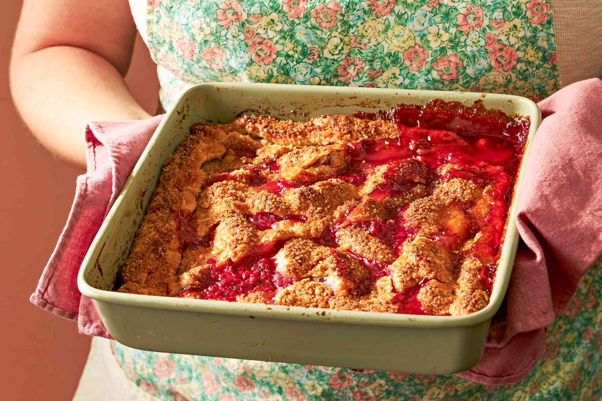 someone holding a casserole dish with peach and raspberry pandowdy with a kitchen towel