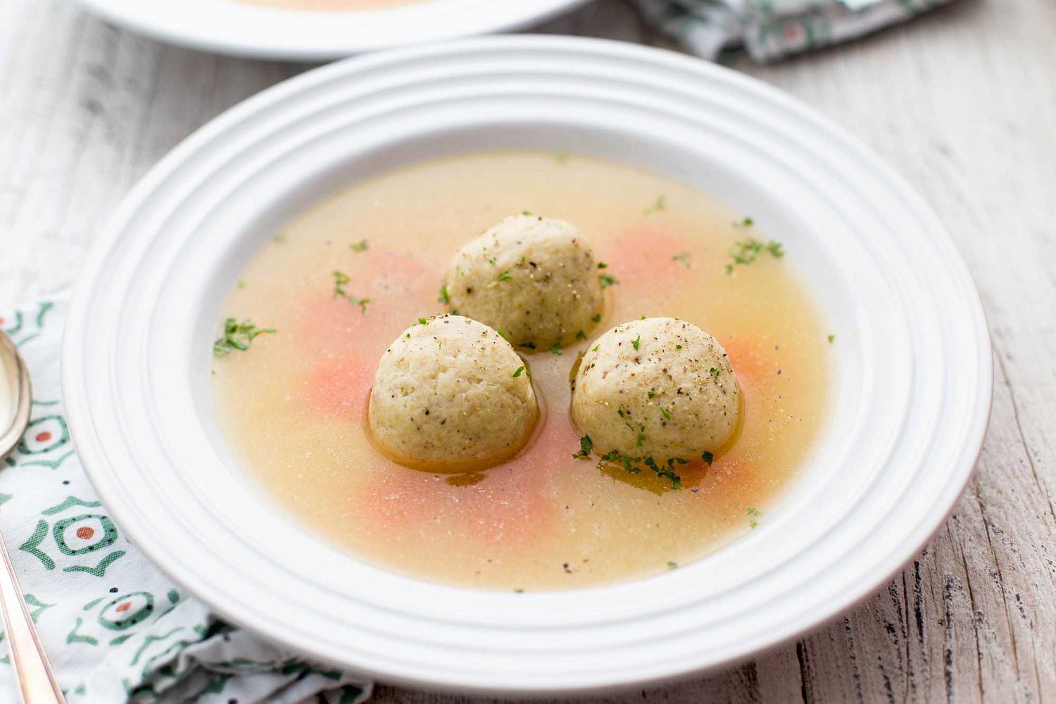 A bowl of matzo ball soup with three matzo balls