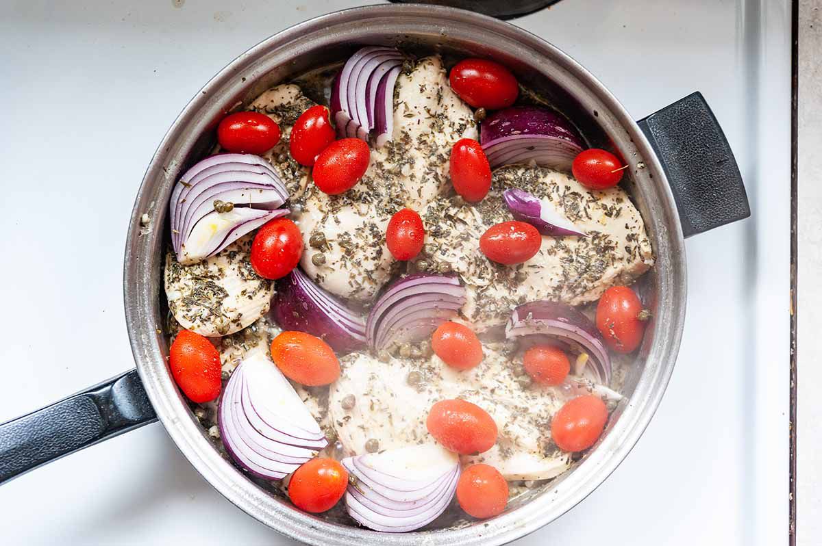 Italian Chicken Recipe in Skillet-top down shot of a silver skillet filled with chicken breasts, grape tomatoes, and red onions