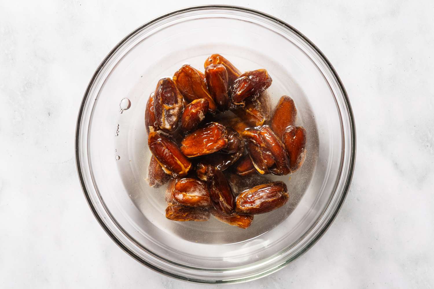 Halved dates soaking in water in a glass bowl
