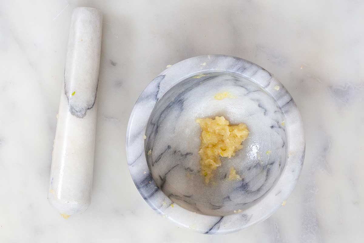 A pestle and mortar with garlic smashed inside.