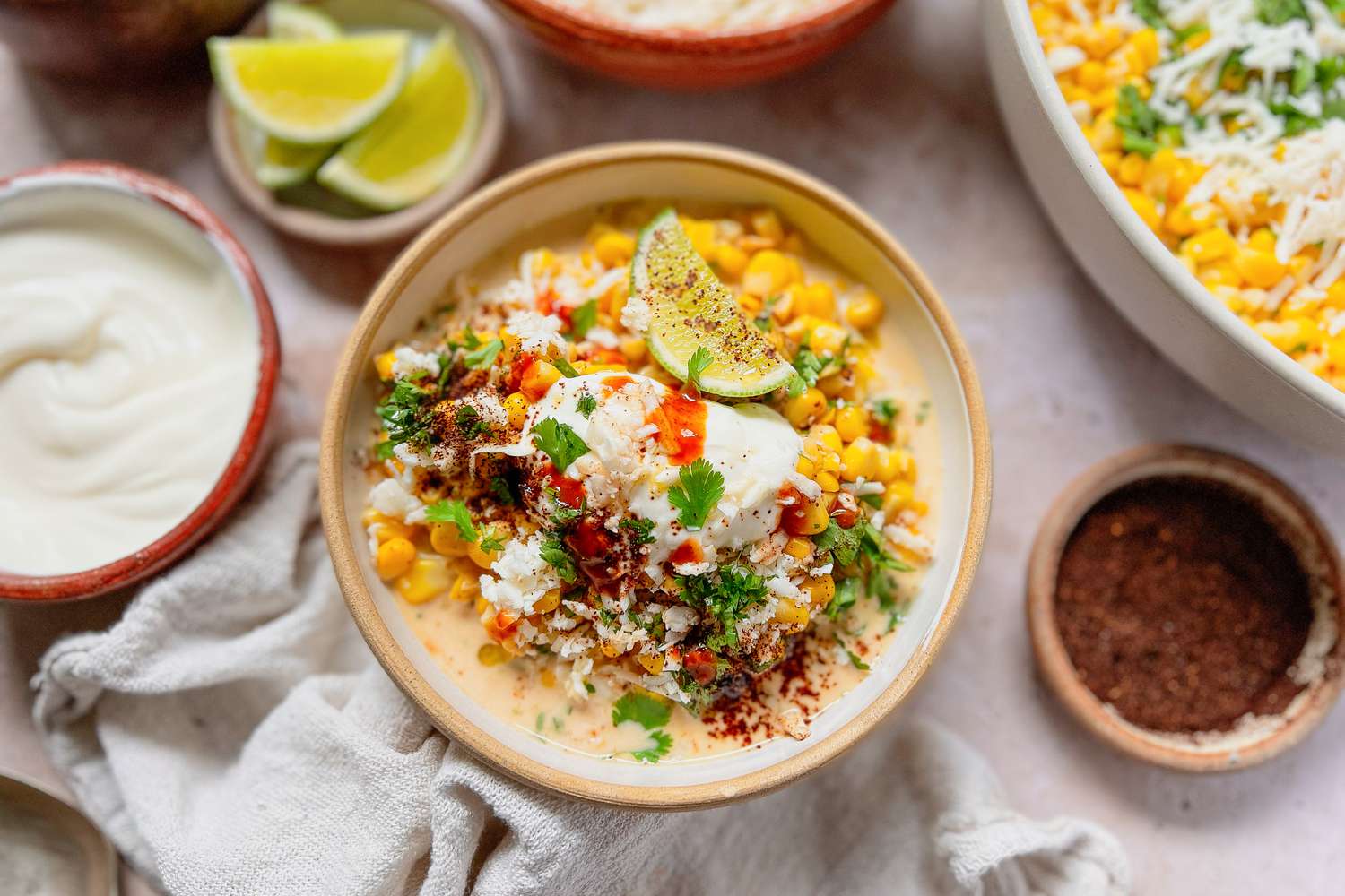 Bowl of Esquites Topped with Cilantro, Cotija Cheese, and Ancho Chile Pepper Surrounded by Bowls of Toppings