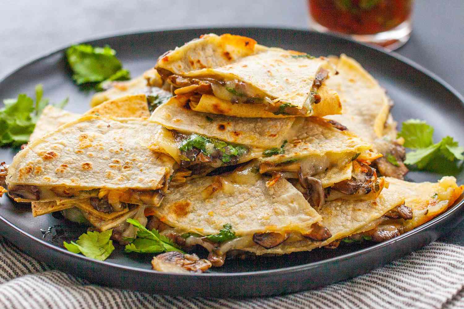 Vegetarian Quesadilla Recipe -close up of cheese and mushroom quesadillas stacked on top of each other with a jar of red salsa in the background.