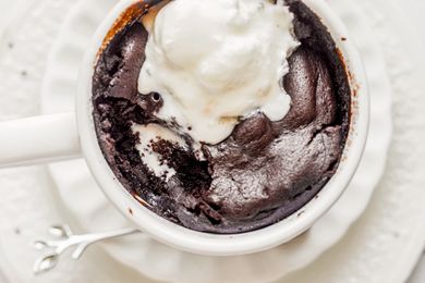 A brownie in a mug topped with a scoop of ice cream served on a plate with a small spoon