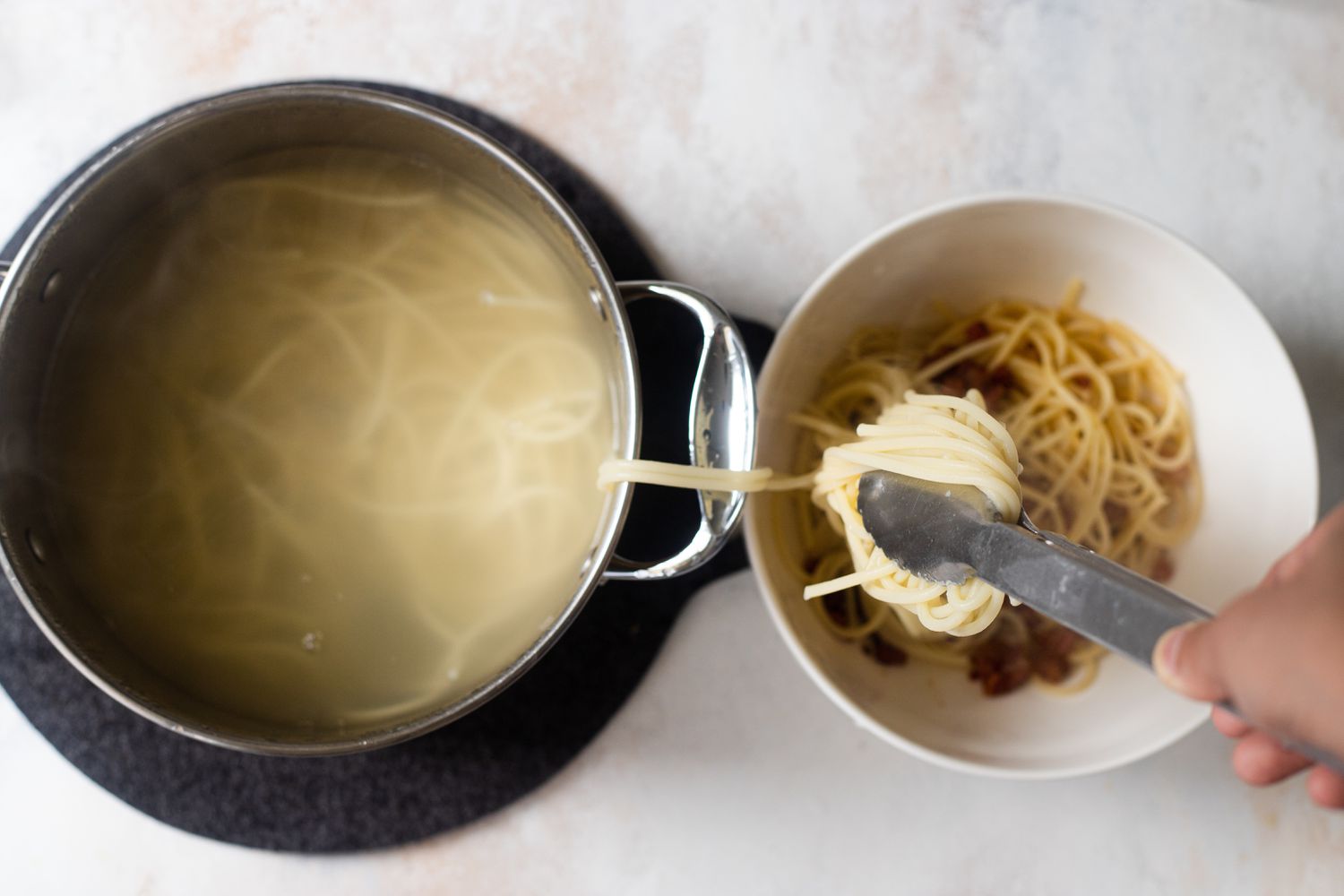 A pot of pasta with tongs moving the pasta to a bowl.