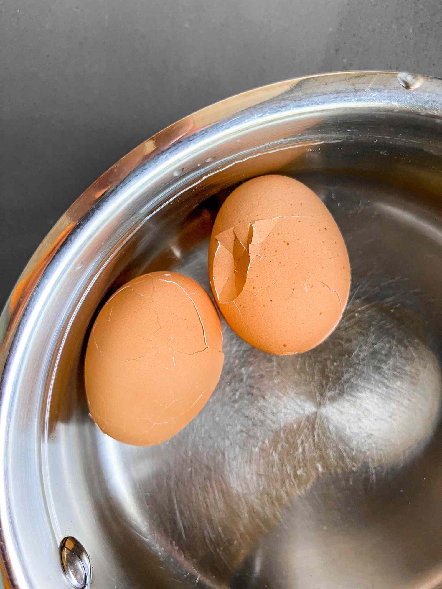 two hard boiled eggs with cracked shells floating in water in a pot