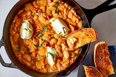 Overhead shot of Tuscan butter beans in a skillet topped with dollops of ricotta toasted bread on the side