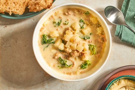 A bowl of sausage kale and potato soup served with bread and grated cheese