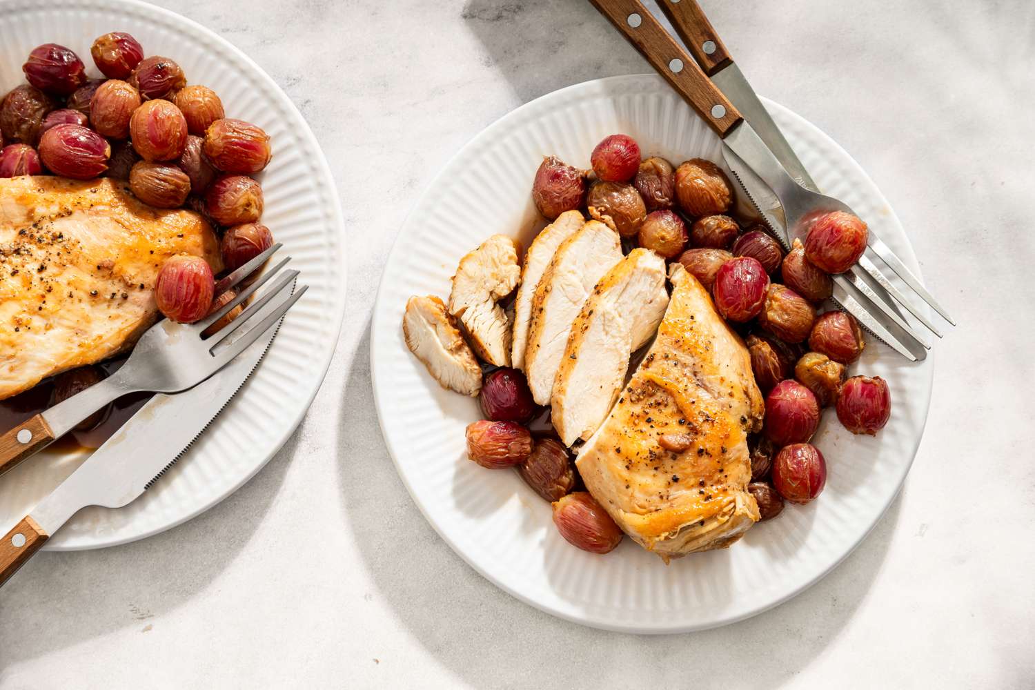 Plates with honey balsamic chicken served with roasted grapes accompanied by forks and knives