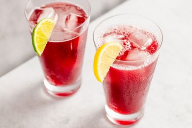 Two glasses of a red beverage garnished with lime and lemon wedges placed on a white surface