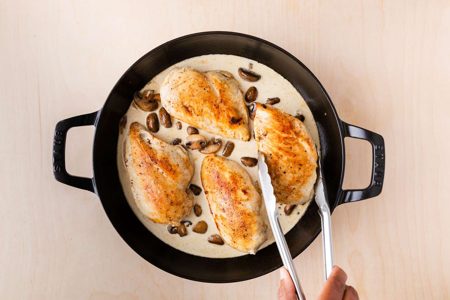browned chicken breasts being added to cream sauce with mushrooms in large cast iron skillet for halved button mushrooms browning in a large cast iron skillet for Chicken Supreme