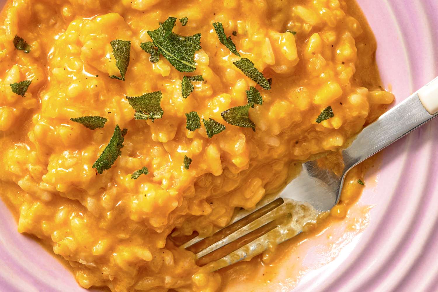 A plate of creamy pumpkin risotto garnished with sage leaves with a fork partially embedded in the dish