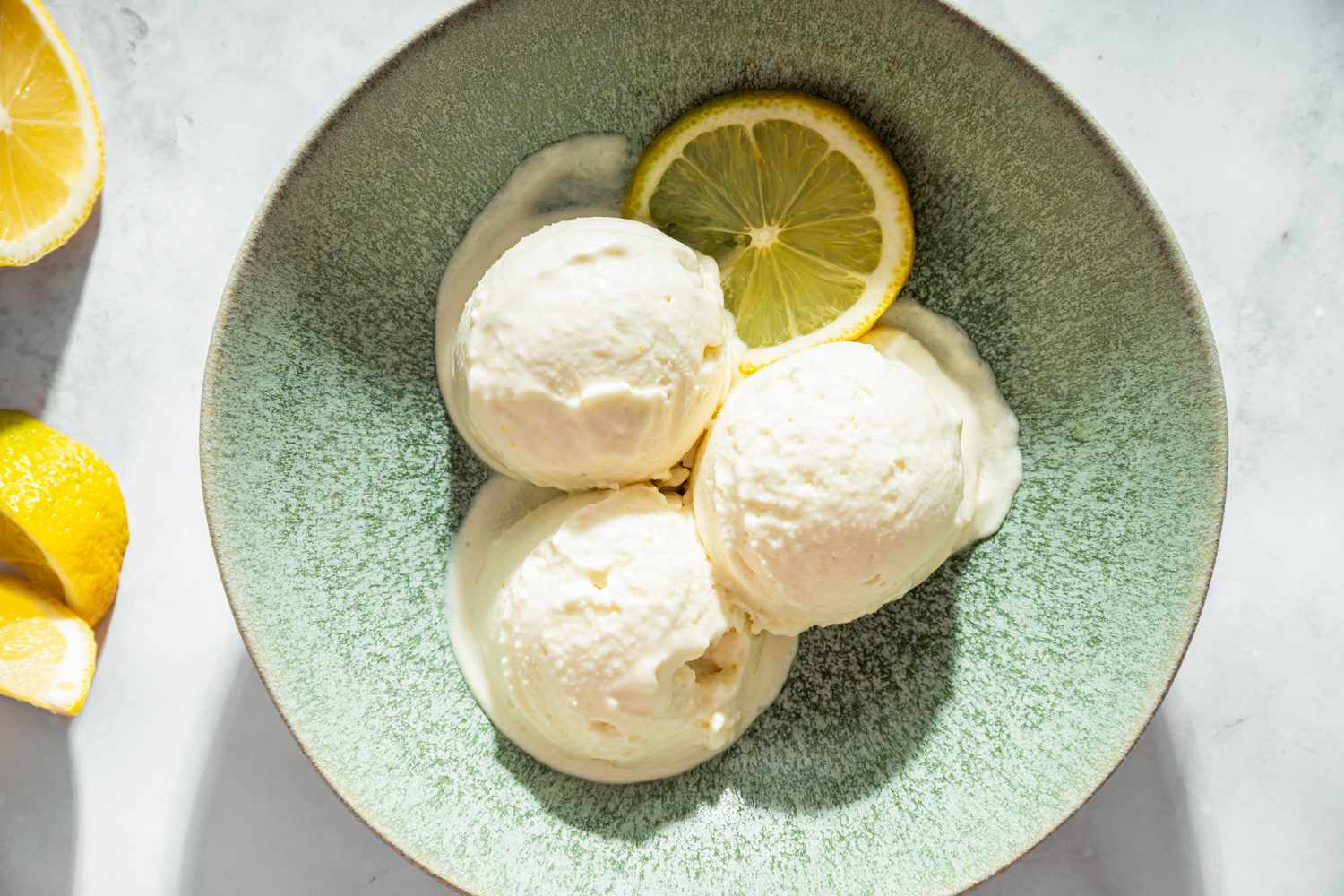 Bowl containing three scoops of lemon coconut sorbet garnished with a lemon slice
