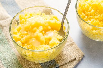 Glass bowls of pineapple coconut granita with spoons, set on a textured cloth